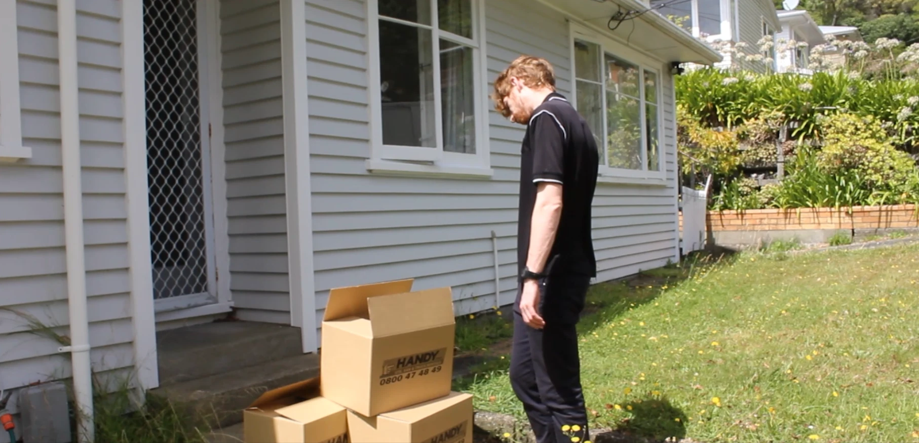 Person standing on front garden looking at pile of cardboard boxes ready to move
